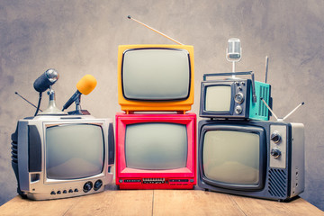 Retro old TV set receivers and microphones on table front textured concrete wall background....