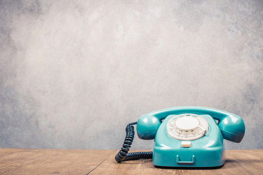 Retro old mint green telephone on wooden table front textured grunge concrete wall background. Vintage instagram style filtered photo