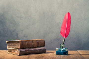 Vintage red quill pen with inkwell and old books on wooden table front concrete wall background. Retro instagram style filtered photo © BrAt82