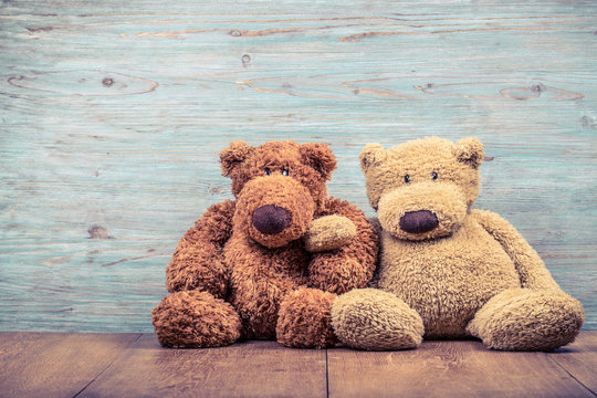 Pair of retro Teddy Bear toys sitting near old textured wooden wall background. Vintage instagram style filtered photo