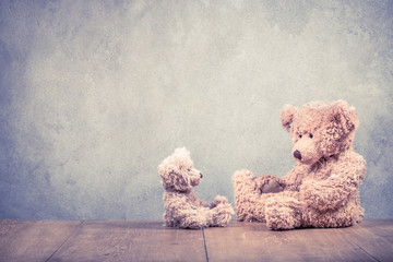 Two retro Teddy Bear toys family: parent with baby front concrete wall background. Parenthood concept. Vintage instagram old style filtered photo