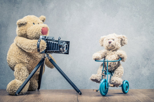 Teddy Bear photographer with old retro outdated film camera making photo of little model on toy bicycle concept. Vintage instagram style filtered photography