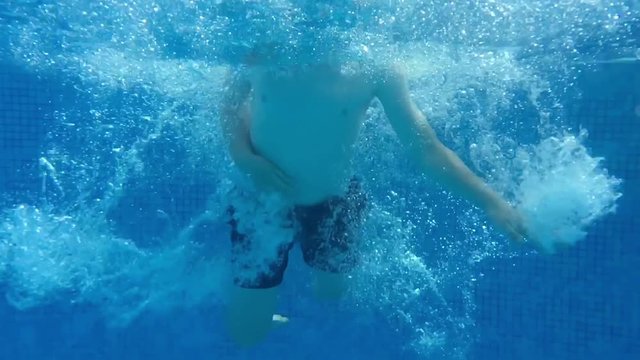 Young boy diving into swimming pool and touching the bottom with his hands