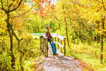 Young man leaning on small wooden bridge in autumn smiling thinking