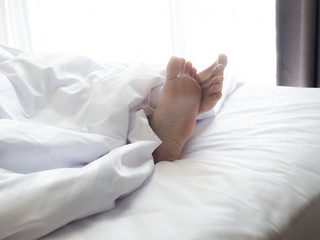Feet of sleeping woman in white bed room.feet of a young woman lying in bed close up.