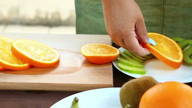 A woman is running a knife with an orange, which is on a cutting board. Full Hd shot with dolly from left to right.