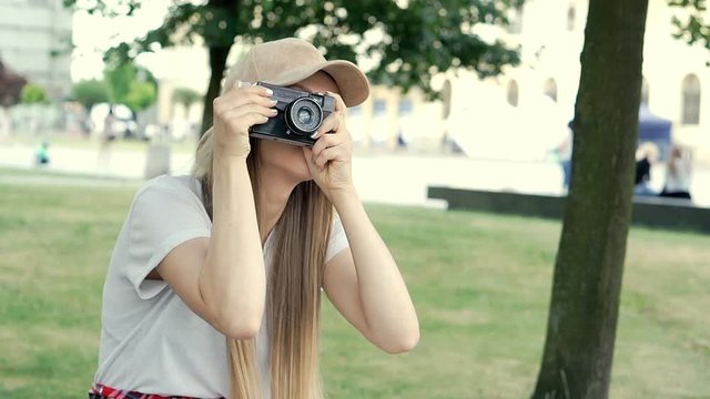 Pretty stylish girl doing photos on old camera in the park and smiling, steadycam shot
