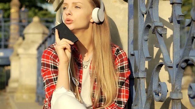 Pretty girl in checked shirt whistles while listening music, steadycam shot
