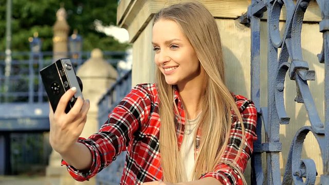Blonde girl in checked shirt doing selfies on old camera, steadycam shot
