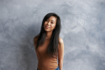 Indoor portrait of amazing charming young Asian female with long black hair, smiling shyly with...
