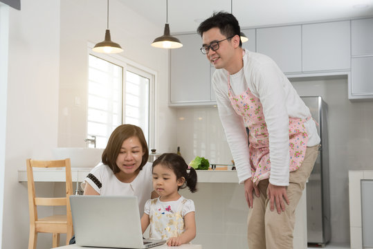 asian mother surfing internet with daughter while father cooking