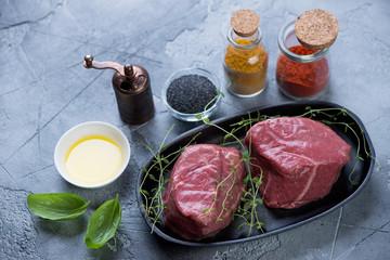 Couple of raw fresh medallion beefsteaks with seasonings on a grey stone background, studio shot