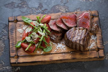Grilled medallion beefsteaks with asparagus and tomato salad on a rustic wooden serving tray, studio shot