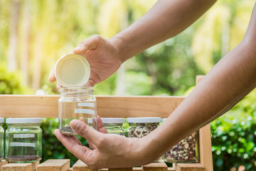 Hand holding a jar with seeds inside,on wooden shelves.Ecology conserve concept.