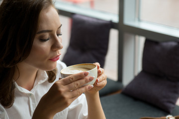 Pretty girl enjoys a fragrant coffee and sweet cake sitting in coffee house. Business woman resting during break.