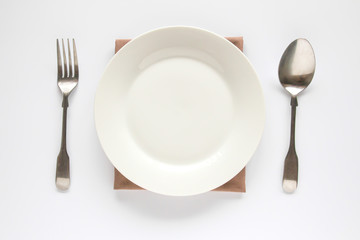 A white plate with silver fork and spoon isolated on white background.