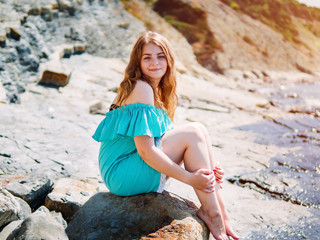 girl in a turquoise dress sitting on a rock by the sea
