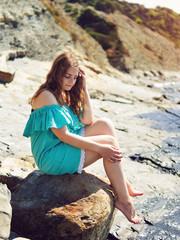 girl in a turquoise dress sitting on a rock by the sea