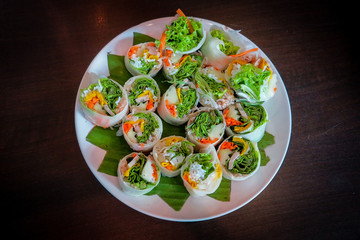 Salad roll on a white plate with a banana leaf on a wooden table.