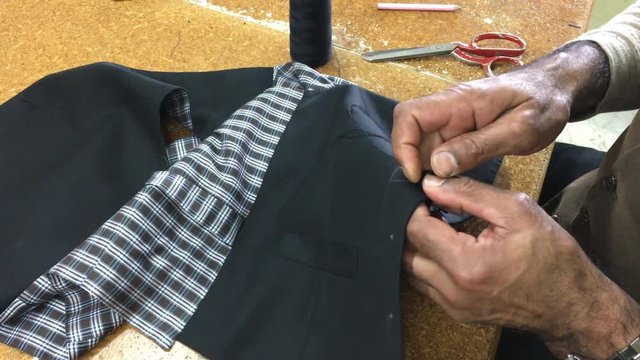 Hands of professional tailor using buttonhole machine on fabric in traditional tailors shop. Real people