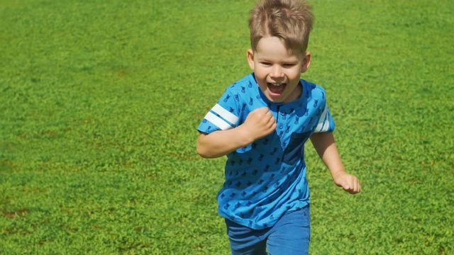 Little boy running across the beautiful green field in summer, very light and happy scene