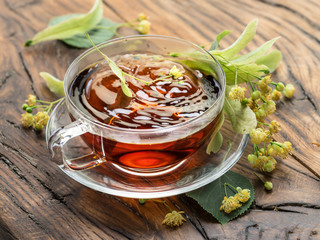 Cup of linden tea and lime flowers on the wooden table.