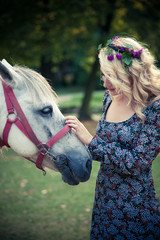 young boho style woman pat horse in park summer day