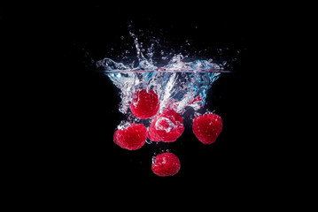 Bunch of raspberries splashing into water surface. Isolated on a black background