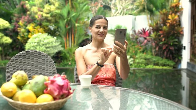 Attractive woman looks happy while doing selfies on smartphone in exotic place, steadycam shot
