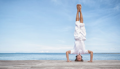 Young man doing yoga exercise - headstand, on a beautiful tropical beach - Powered by Adobe