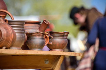 A lot of clay pots standing on a table and blurry man wearing the medieval costume at international knight festival Tournament of Saint George