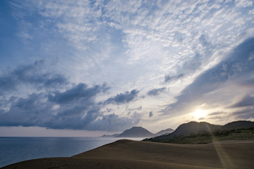 Fototapeta na wymiar 朝日が砂丘に射し込み始める夏の朝の海・島・空の協演