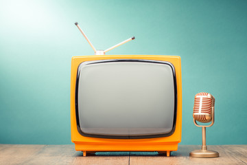 Retro old TV receiver and golden microphone on table front gradient mint green wall background. Broadcasting concept. Vintage style filtered photo