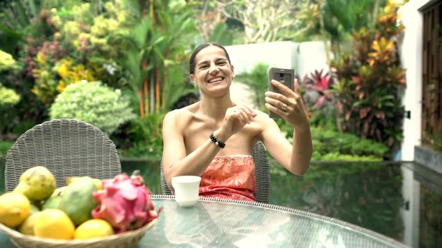 Attractive woman doing selfies on smartphone in exotic place and smiling to the camera, steadycam shot
