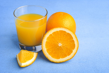 Fresh orange juice in the glass next to the orange slices on blue wooden table
