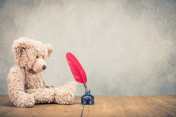 Retro Teddy Bear toy with red quill pen in the inkwell front concrete wall background. Vintage instagram old style filtered photo