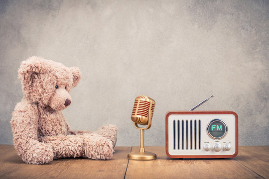 Retro Teddy Bear toy with golden microphone and fm radio receiver front concrete wall background. Listening music concept. Vintage old instagram style filtered photo