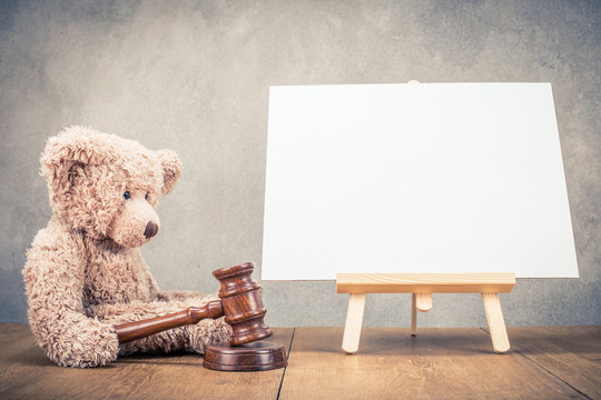 Teddy bear toy with auction gavel and easel for painting with canvas blank front concrete wall background. Retro instagram old style filtered photo