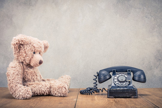Teddy Bear toy and old retro black rotary telephone front concrete wall background. Vintage instagram style filtered photo