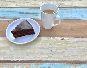 Closeup A white cup of hot coffee with A piece of chocolate cake on white saucer set on pastel colorful wooden background. Top view with Copy space. Selective focus.