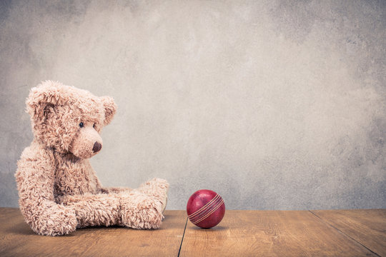 Retro Teddy Bear sitting alone and leather toy ball front old concrete wall background. Vintage instagram style filtered photo