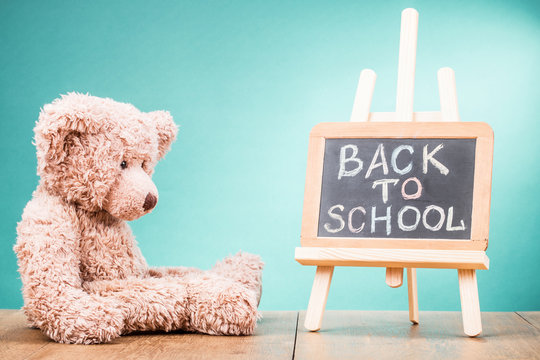 Retro Teddy Bear toy and Back to School written on a blackboard front gradient aquamarine wall background. Vintage instagram style filtered photo