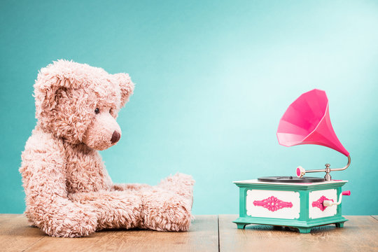 Teddy Bear toy sitting at the wooden floor with retro gramophone front gradient aquamarine background. Vintage old instagram style filtered photo