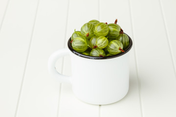 Fresh green gooseberries in an enamel mug on white table