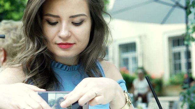 Attractive woman checking her photos on smartphone and showing them to the camera, steadycam shot
