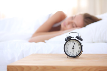 Young sleeping woman and alarm clock in bedroom at home. Young sleeping woman.