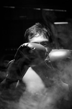 A man wore boxing gloves with smoke for boxing match. Selective focus on boxing gloves. Black and white image.
