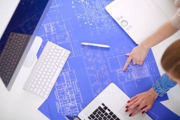 Two young woman standing near desk with instruments, plan and laptop.