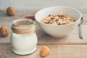 Jar of milk or plain yogurt with a spoon and a white bowl with granola or muesli in the background. Healthy breakfast top view composition