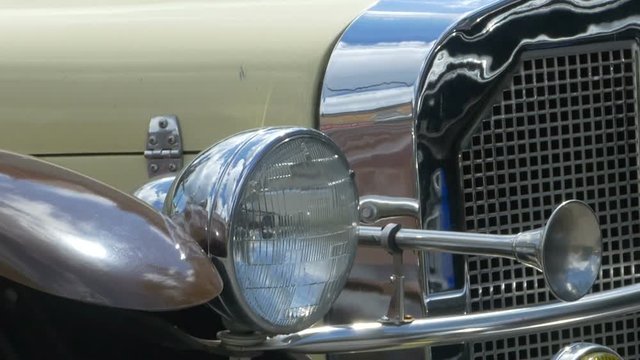 Pan shot the front of a vintage car with headlights and horns.